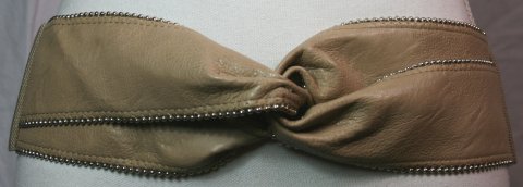 8 cm. bredt beige elastik bælte. Foran kunstlæder med nittekant, der laver en knude, bagpå elastik der lukkes med tryklåse. One Size.